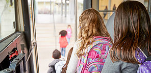 Des enfants sortent d'un bus scolaire, cartables sur le dos